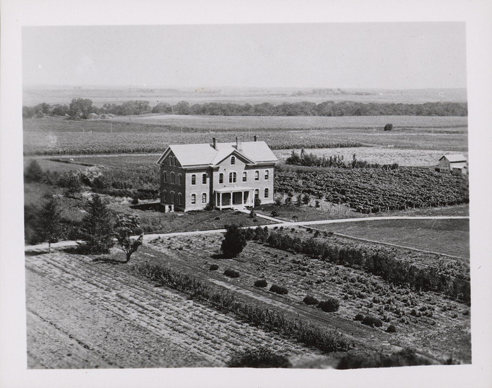 Photograph of North Hall on the Iowa State campus, viewed from Main looking northeast. The image shows a brick building situated within an agricultural landscape, surrounded by cultivated fields, garden plots, and open land. Annotation: "North Hall, neg 05123."