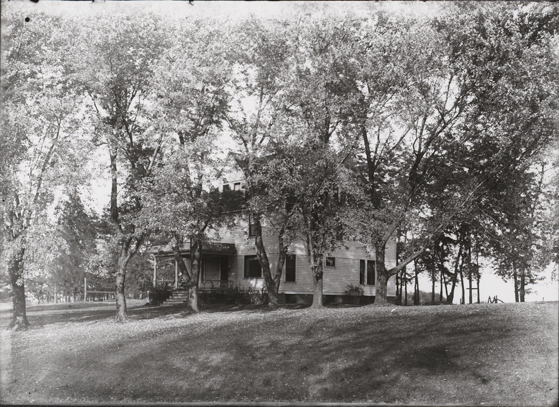 Photograph of Norton House on the Iowa State campus, showing the front and side elevations of a two-story residence partially obscured by mature trees. The building features a porch and is situated on sloping, landscaped grounds. Annotation: "Norton House. glass neg #1325. Lizzie May Allis house, 1900â€“1907, then Coover, then Gray Cottage, then Norton House. Moved twice on campus. Razed in the early 1980's. n.d."