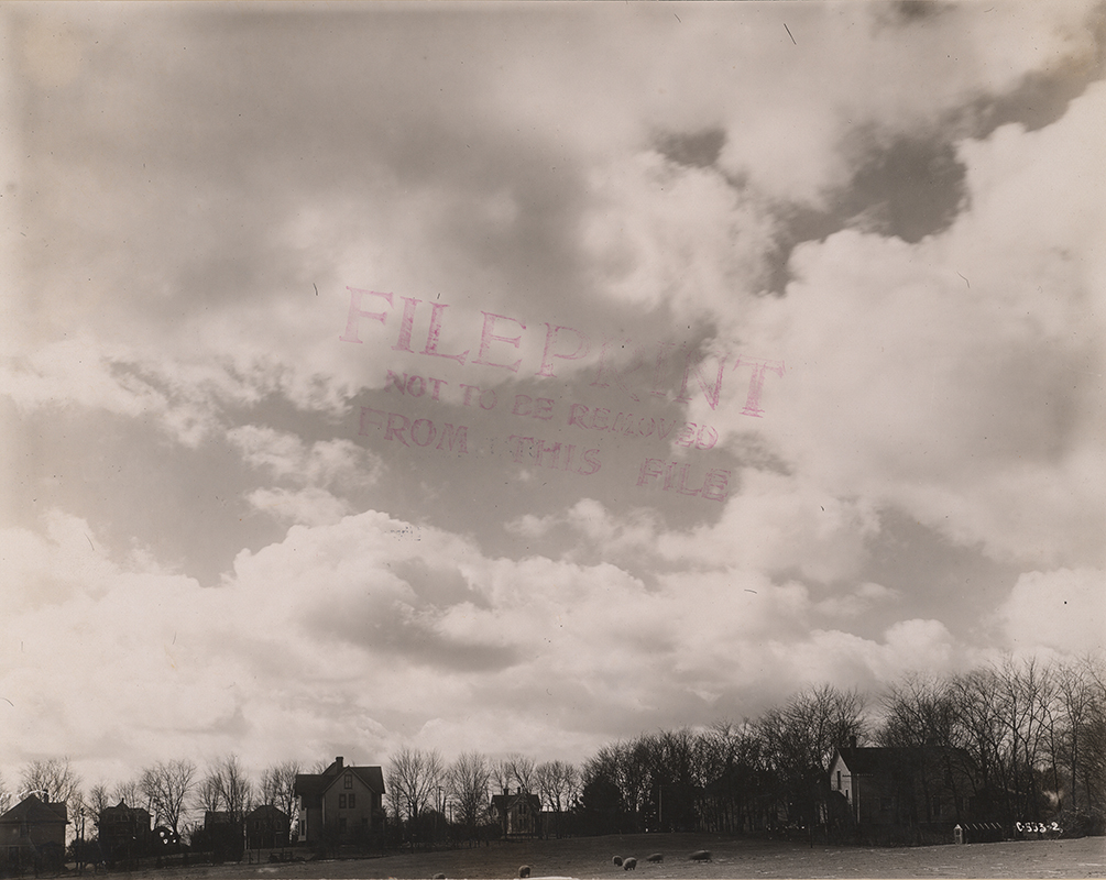 Photograph of a broad landscape view on the Iowa State campus featuring Pope Cottage among several other residential buildings. The image shows multiple houses spaced across open ground, with leafless trees in the background and a large sky filled with clouds dominating the upper portion of the photograph. Annotation: "Pope Cottage."