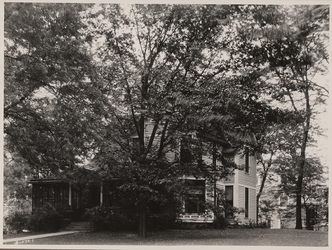 Photograph of Coburn House in 1921. The house is largely obscured by trees. Caption reads "Gertrude Coburn Practise House formerly Mary B. Welch House at one time the home of Herman Knapp family. A practise [sic] house in 1921."
