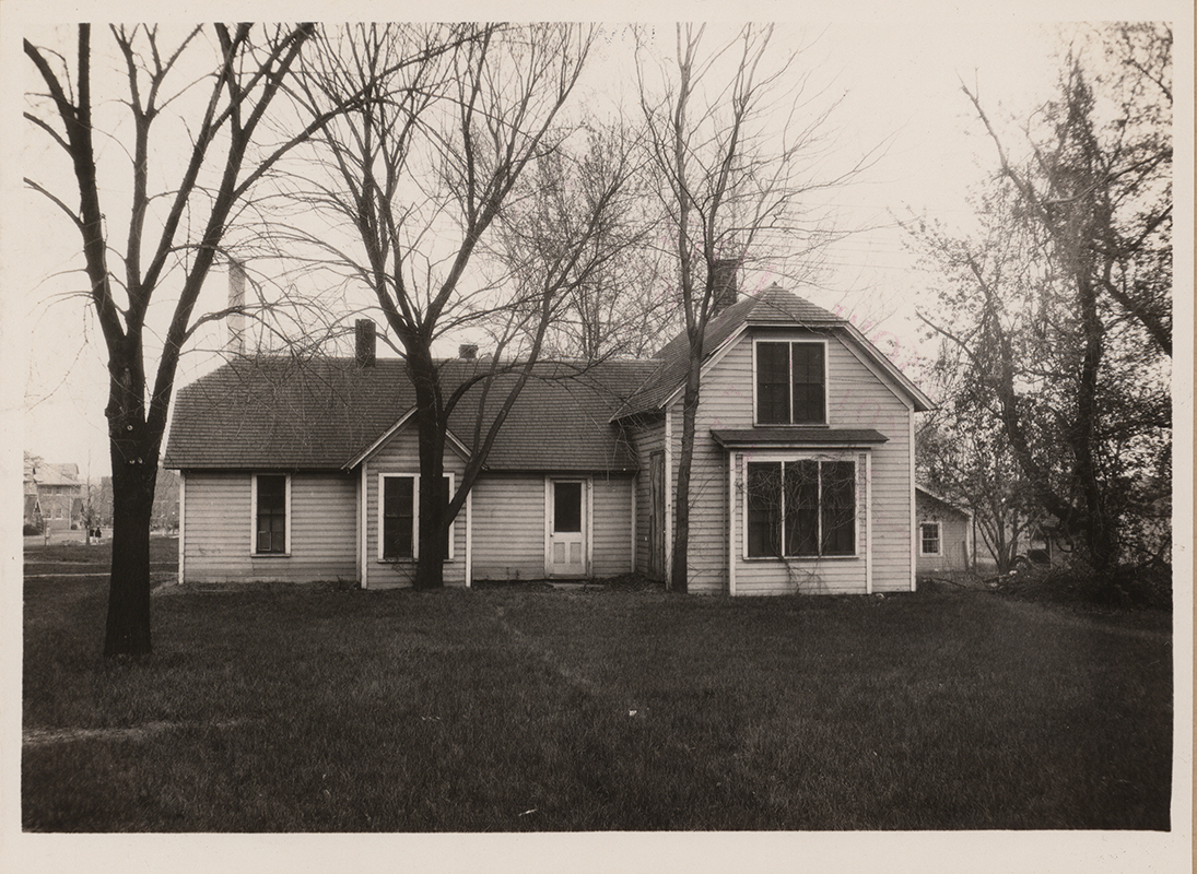 Photograph of the first creamery building, facing east. In the left background, the judging pavilion and the power plant are visible. The creamery is a one-story building. Leafless trees are in the foreground.
