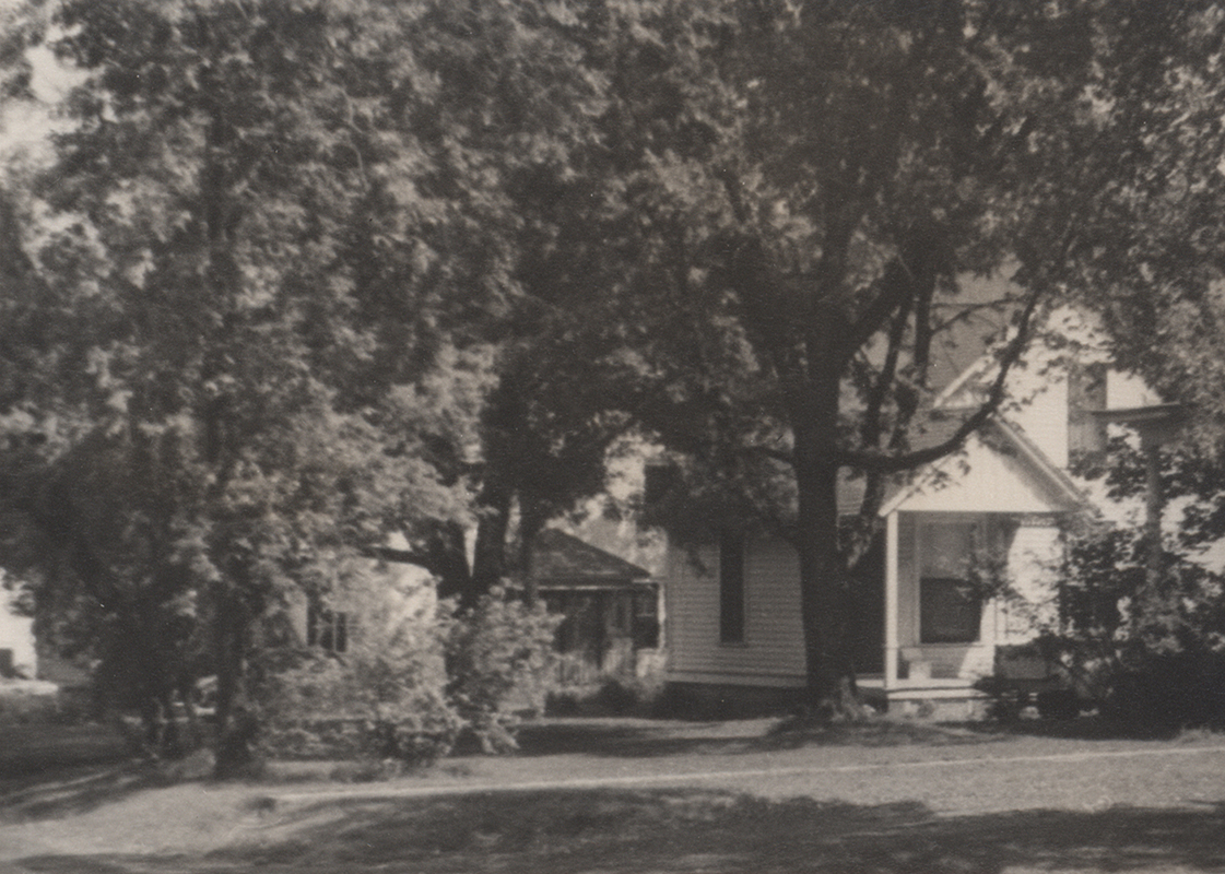 Photograph of the 2nd Teamster's Cottage. The buildings are mostly obscured by large, leafy trees.