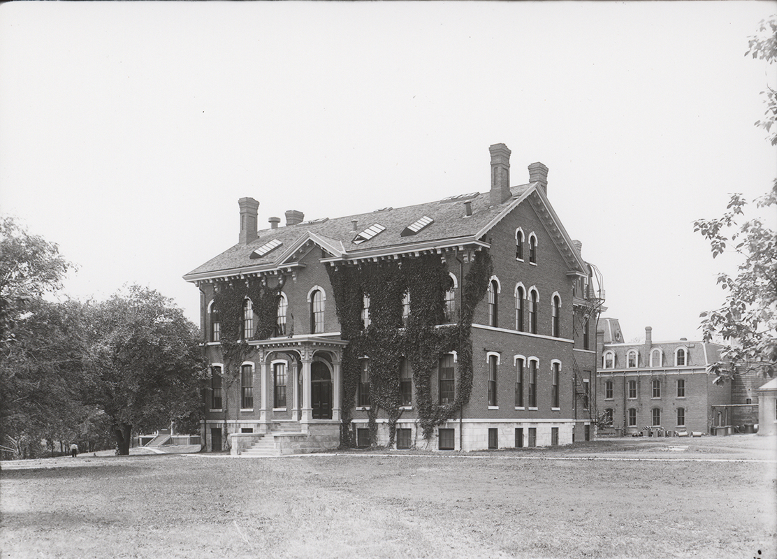 Photograph of the Chemical and Physical Laboratory. It is a two-story brick building with ivy growing on the front. The Laboratory of Mechanics is visible in the right background.