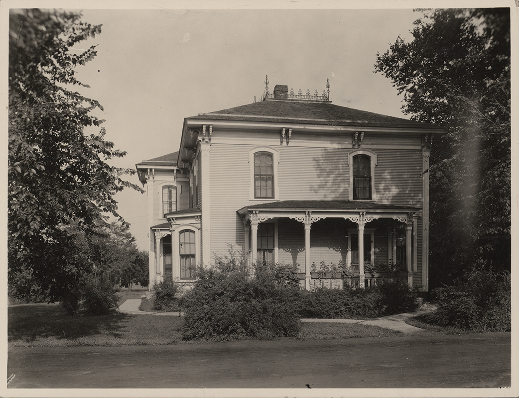 Photograph of Mortensen Cottage. The photo provides a side view of the house. It is a two-story house with a side porch. Many bushes and greenery full the space around the house. The caption reads "Old residence of Prof. J. L. Budd on site of Dairy Industry. Sold by Budd to College about 1890. Prof. Kent lived there, then Dr. Weems, then Prof McKay and then Prof. Mortensen for 17 years."