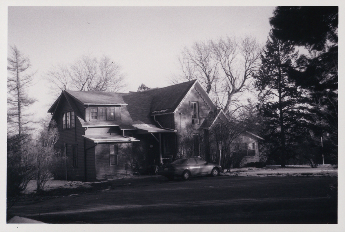 Photograph of Osborn Cottage looking southeast at the rear and west side of the building. A car is parked along the west side of the building facing south.