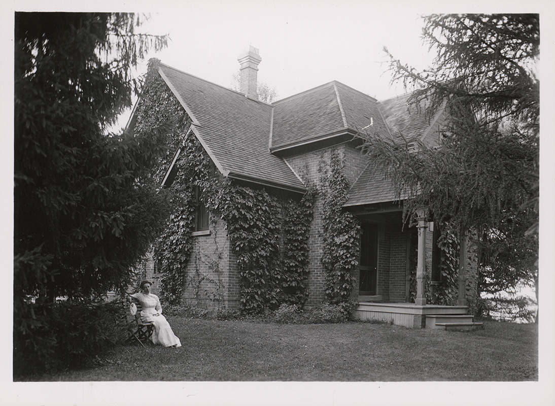 Photograph of Lillian Spray sitting outside the southwest corner of Osborn Cottage. Annotation: ''Mrs. Lillian Spray, housekeeper for Prof. Summers, sitting in front of the Osborn Cottage when the Summers family lived there. Around 1906.''