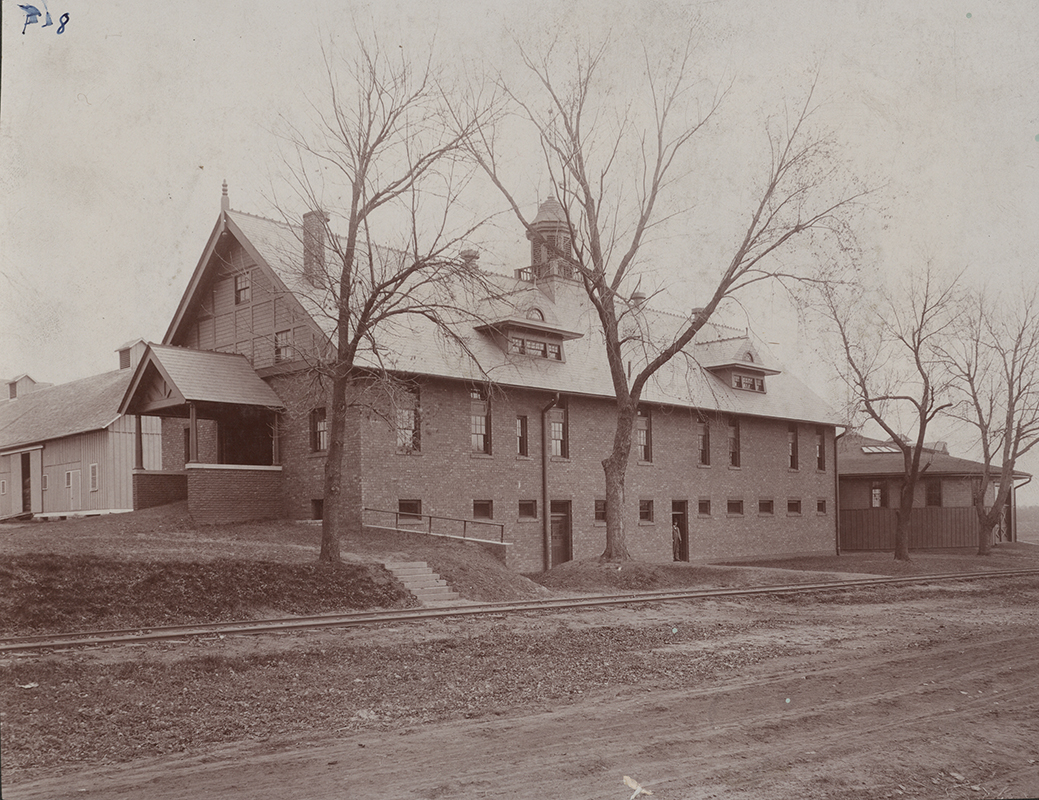 Photograph of the southwest corner of Landscape Architecture when it was the Horse Barn. The Cattle Barn can be seen to the north (left), and the Theater Workshop (when it was the Judging Pavilion) can be seen to the east (right). Dinky tracks run along the south (foreground) of the buildings.