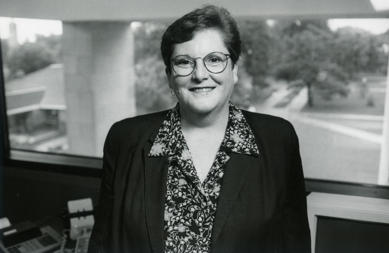 Nancy Eaton, Dean of the Library, is standing in her fourth floor office with a view of the Hub and campanile in the background.