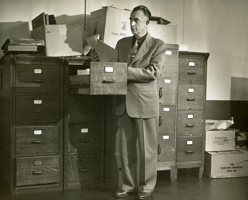 Robert W. Orr, Professor and Director of Libraries, is examining files in a wooden filing cabinet in the library.