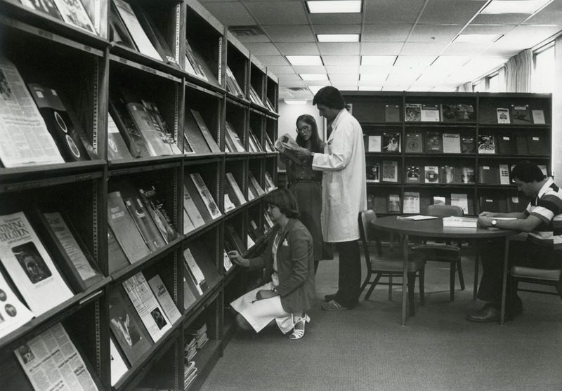 Susan Knippel (kneeling) and Linda Meetz (standing), library assistants, are assisting graduate student, V. Miletic, in the Veterinary Medical Library. John Hogan is reading at the table.