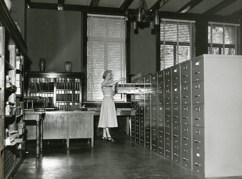 Dorothy Kehlenbeck, curator of the College Historical Collection is standing before an open file cabinet drawer examining papers. The collection is located in the corner of the Faculty Reading Room 105.