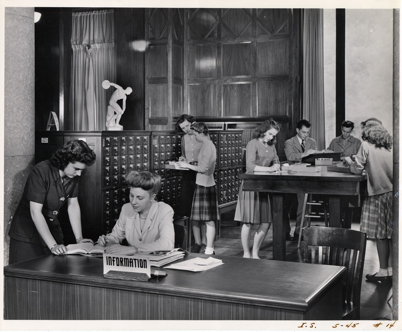 Ida Robertson, cataloger, helps student look up reference in card file. Kathryn Renfro, cataloger, at information desk looks up some information in a reference book.