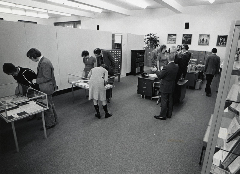 An open house in Special Collections is attended by several people. The attendees are talking together or examining the displays.