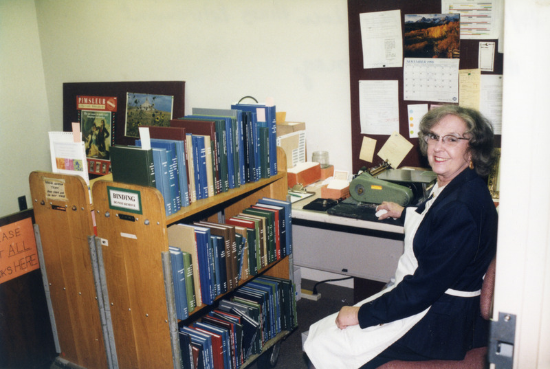 Mary Lou Hines is seated next to a book truck filled with volumes waiting for processing. The photograph was taken as part of Library Staff Association's retirement tea for Mary Lou Hines held on November 11, 1998.