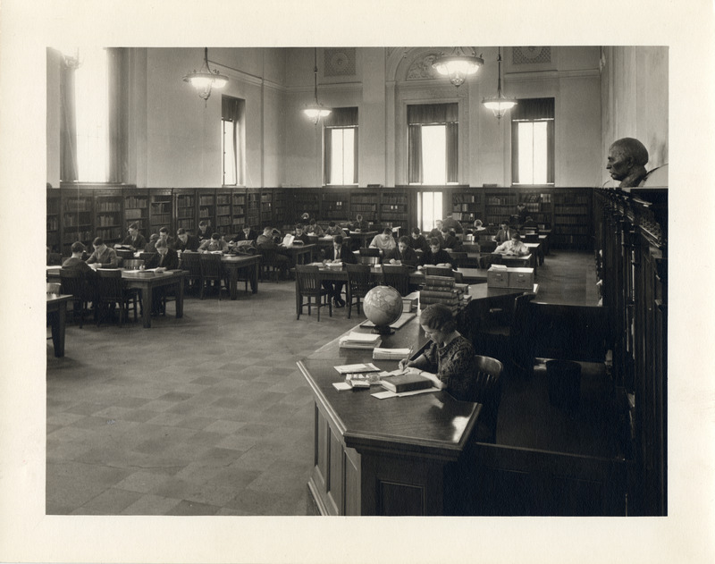 Students study in the library Reference Room (currently called Periodical Room), while a librarian works at the reference desk.