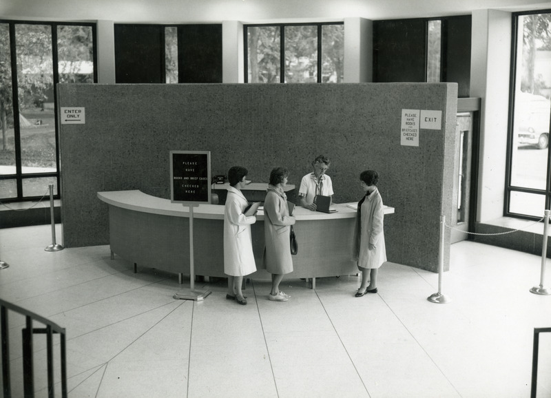 A library monitor, Mrs. Isabel Matterson, checks the books of three women inside the library Rotunda (south) entrance.