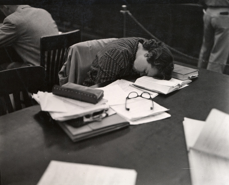 A female student puts her head down to nap on her books at a table in the library.