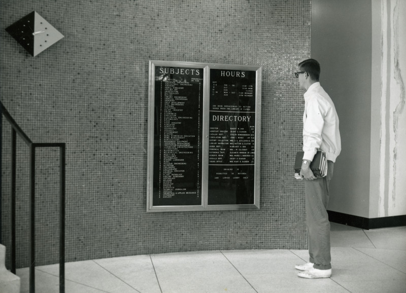 A male student looks at the library building directory on the wall inside the Rotunda (south) entrance.