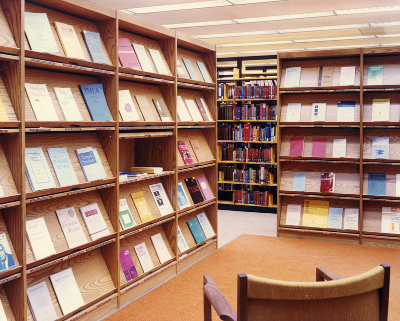 A periodical space in the library features slanted display shelving for current issues, orange carpeting, and a modern chair.