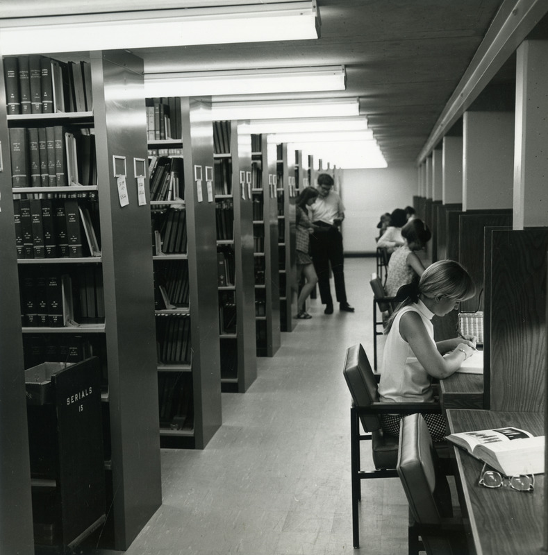 Students at study carrels along the wall of one of the newly completed 2nd Addition tiers in the library, while the shelves are in the process of being filled and labeled with call number ranges.