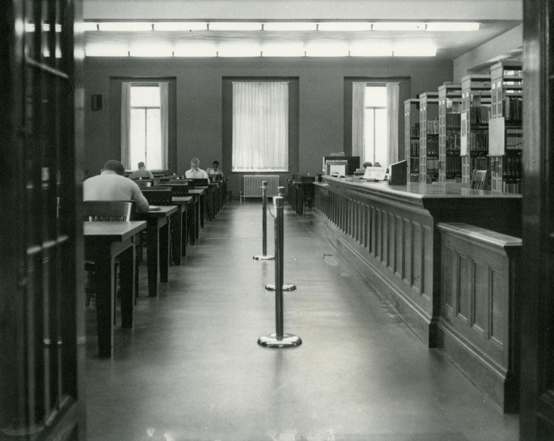 A long wooden desk with shelves behind it fills one side of the Reserve Room (currently Room 198), with students studying at tables on the other side.