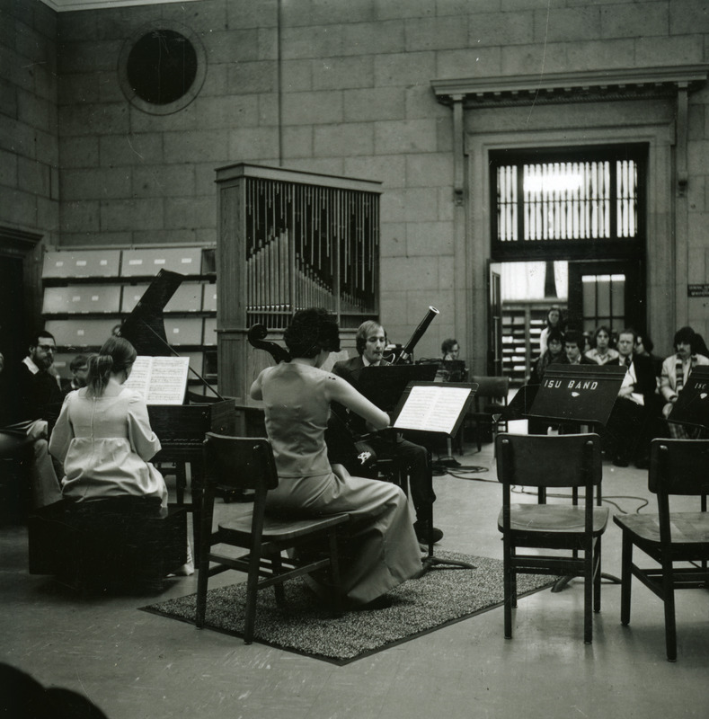 The first Baroque concert in the library is held in the upper rotunda lobby outside the Periodical Room, Dec. 7, 1973. Performers in formal dress play instruments including a bassoon, a cello, and a harpsichord.