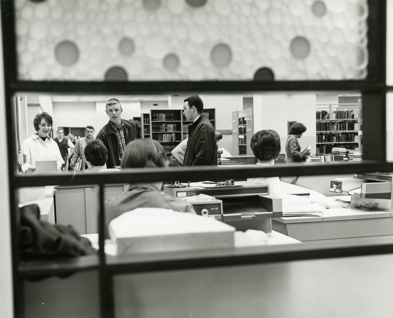 Students and staff at the reference desk are viewed through a decorative screen embedded with colorful circles.