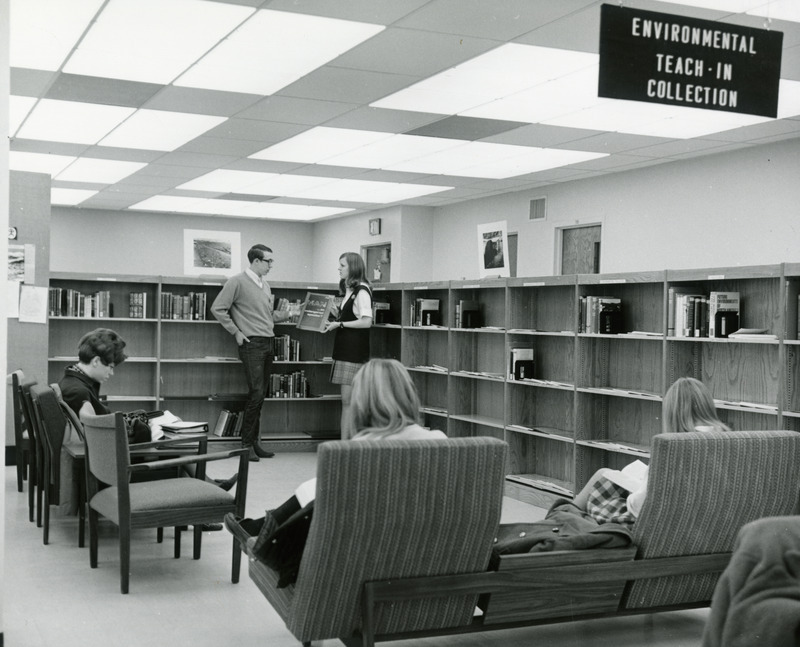 Two students hold a book on "Man: An Endangered Species?" in the Environmental Teach-In Collection, while other students study nearby.