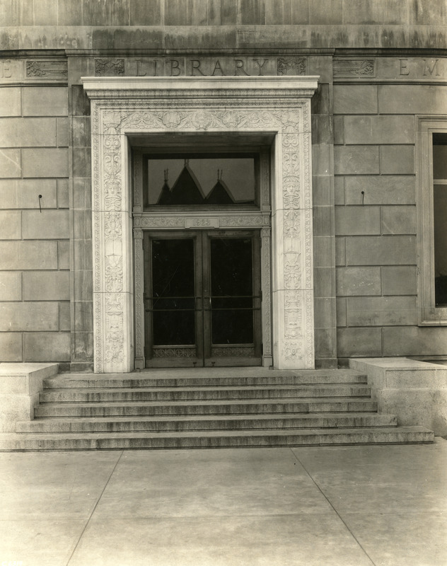 The year 1923 is engraved above the doorway of the east entrance to the library. The tower peaks of Margaret Hall are reflected in the glass window above the entrance.