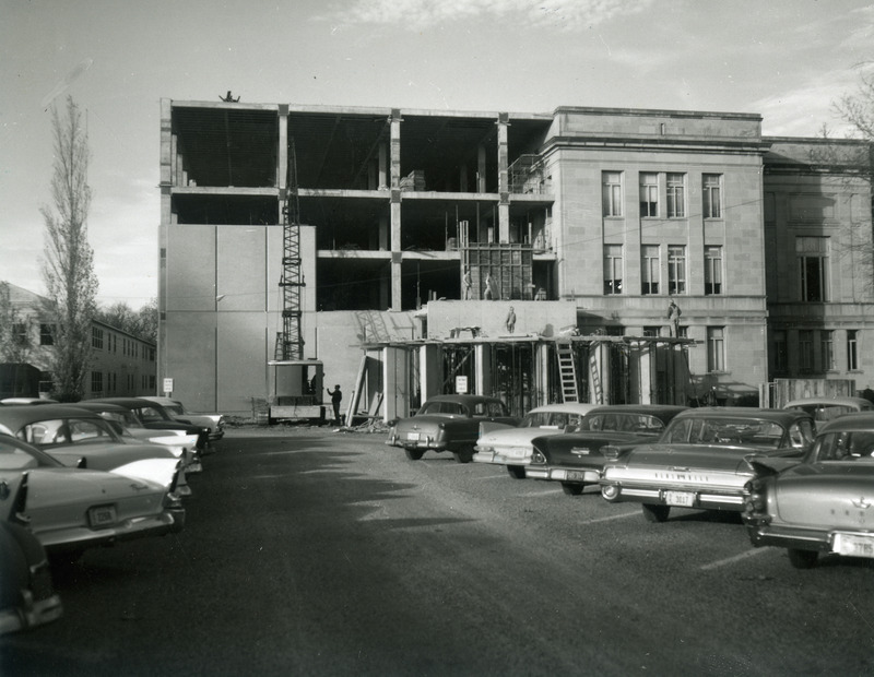 Men are working on the construction site for the 1st addition in this view from the parking lot filled with late 1950 vehicles. The rotunda entrance is beginning to take shape. A war surplus building, Number "N", appears on the far left. It was taken down in 1968 prior to construction of the 2nd addition.