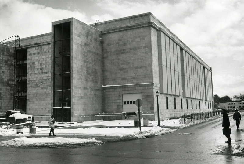 A woman is walking on the snow-cleared sidewalk along the north side of the 2nd addition construction. Scaffolding is still visible on the left. Two men are walking in the driveway on the west side of the addition.