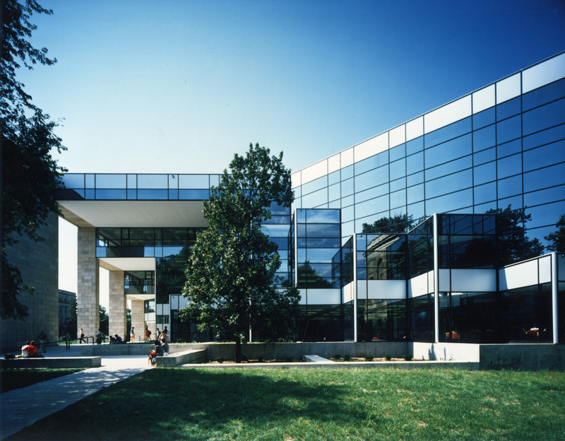 Students are sitting around the entrance to the University Library on a sunny day.