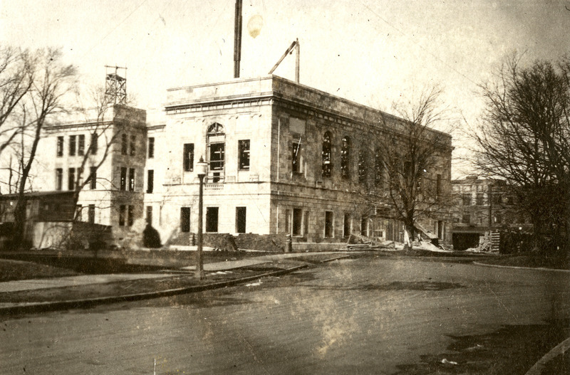 Work continues on the construction of the original library building. Construction materials are laying around the future east entrance to the building. A portion of Gilman Hall can be seen on the right.