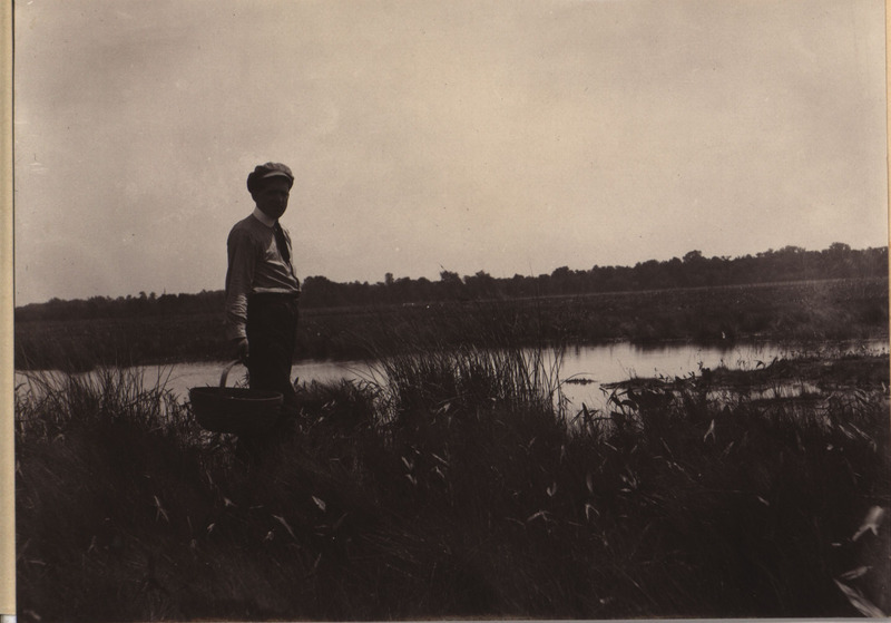 Black and white photograph of Mr. Buchanan holding a basket next to a pond at Hayden Place.