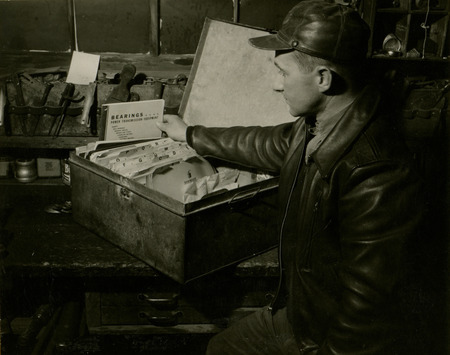 A large steel box containing the instruction manuals for all the farm machinery on the H. B. New Farm is setting on a wooden table. A man is standing beside the box examining one of the manuals.