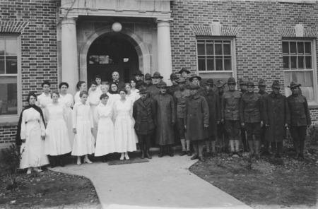 A military corps and hospital staff formal portrait in front of the Student Services Building. Eighteen uniformed men, fourteen uniformed female nurses, and one man in a suit are posed for the photograph.