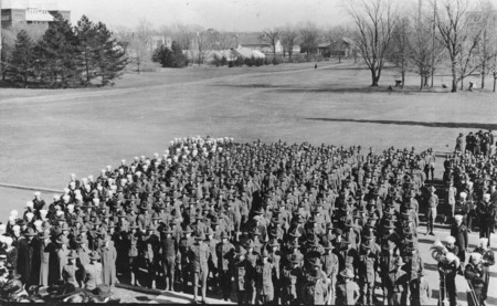 A military parade on November 11, 1918, at Iowa State College. Taken from high on the steps of Beardshear Hall, the photograph shows army and navy personnel in uniform and includes a navy band. A small group of civilians can be seen at the rear of the military units.