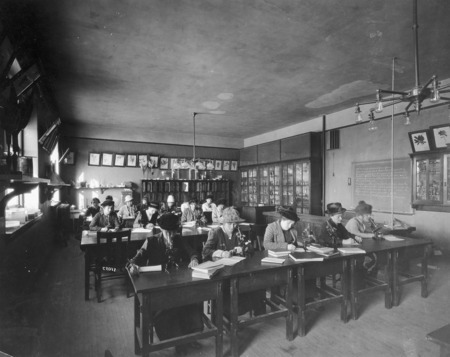 A class of all female students is working in the Botany Lab in Central Building (Beardshear Hall) perhaps completing an assignment written on the blackboard. Books and microscopes are on their desks.