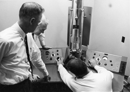 C. Clark Bowen (seated) is operating the electron microscope. Dean Bear, College of Sciences and Humanities (center) and Dean Andre (in the back), College of Agriculture look on.