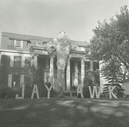 The Theta Delta Chi, Beta Deuteron Chapter, lawn display is located on the front lawn of their house. The central figure of the display depicts the head, arms and torso of a muscular male. The lower part of the figure tapers to a cyclone shape. On either side of this figure the word "Jayhawk" is spelled out in separate letters. The "h" is laying horizontal to the ground.
