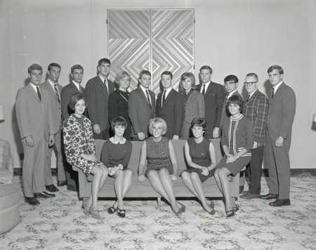 The 1966 Central Homecoming Committee is shown in a formal portrait. Five members are seated on a sofa while the other committee members stand in a row behind them.