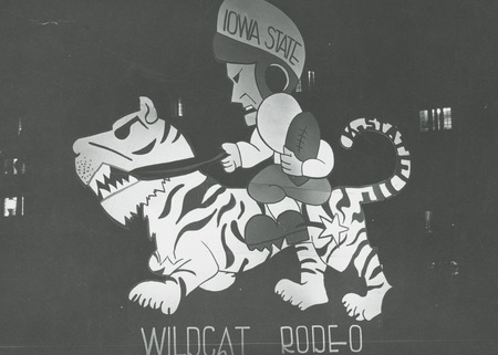 A football figure labeled, "Iowa State' rides a tiger figure that represents the Kansas State University's mascot, the Wildcat. The sign below these two figures reads, "Wildcat Rodeo.".