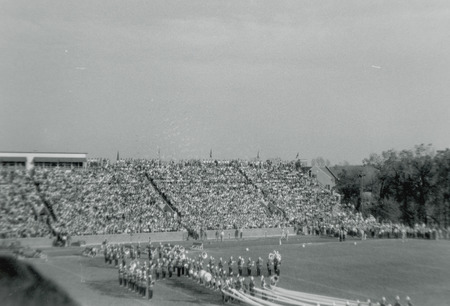 The ISU marching band is in formation on the football field before bleachers that are full of spectators. Several long streamers are stretched between band members.