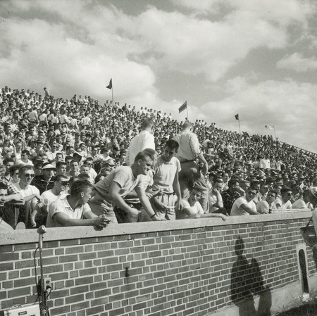 A group of students and other spectators are watching the Homecoming football game.