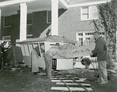 Tau Kappa Epsilon, Epsilon Chapter Fraternity members are working on their lawn display, "Getting on the Victory Train." Three men are sliding a drawing of the ISC coaches and players into the train.