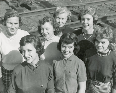 The 1950 homecoming queen candidates are posing in front of a railroad track. They are front row (left to right): Janet Green, Sac City; Rita Dunn (Queen), Sioux City; Betty Skyberg (Attendant), Canton, SD; Back row (left to right): Pat Binder, Barrington, IL; Claire Schubert, Maywood, IL; Ethel Pearce (Attendant), Mesa, AZ; Marlene Sidney, Davenport.