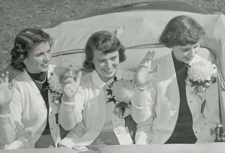 The 1951 Homecoming Queen and attendants are waving from the car. They are from left to right : Ann Bradley (Attendant); Doris Blair (Queen); and Bonnie Helfrich (Attendant).