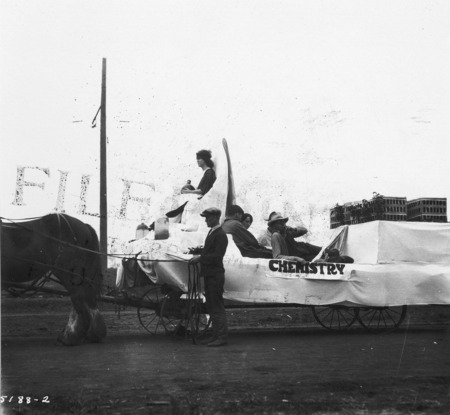 A 1923 VEISHEA Chemistry float. The horse-drawn float is mounted on a flat bed wagon. Viewed from behind, Margaret Hall can be seen in the background. See photographs 1722-3-3 and 1722-3-4 for other views of the same float.