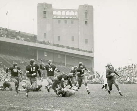 Everett Kischer carrying the ball. A football game being played before a partially filled stadium of spectators.