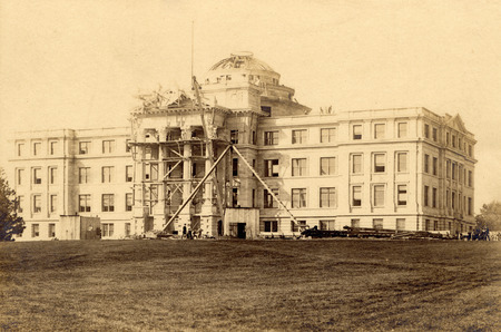 Beardshear Hall under construction. Scaffolding, a construction shack, and equipment are in place. Workmen are present, including several carving the capitals of the columns. The dome is unfinished. The photo shows the east side of the building.